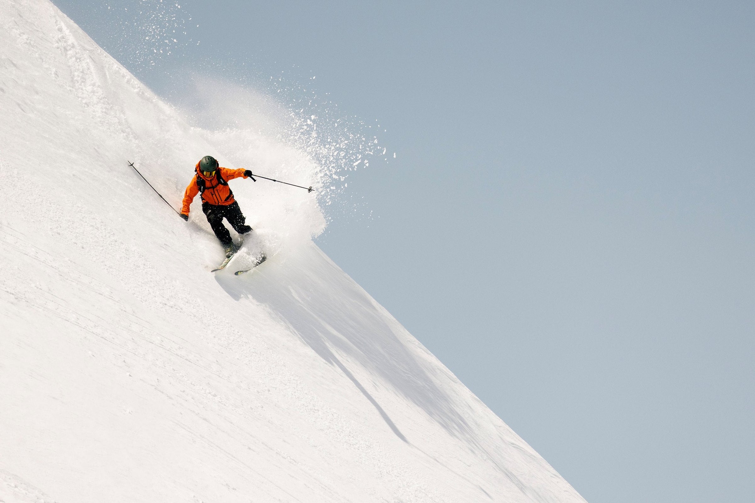 person skiing on a steep snowy slope wearing an orange jacket and a helmet