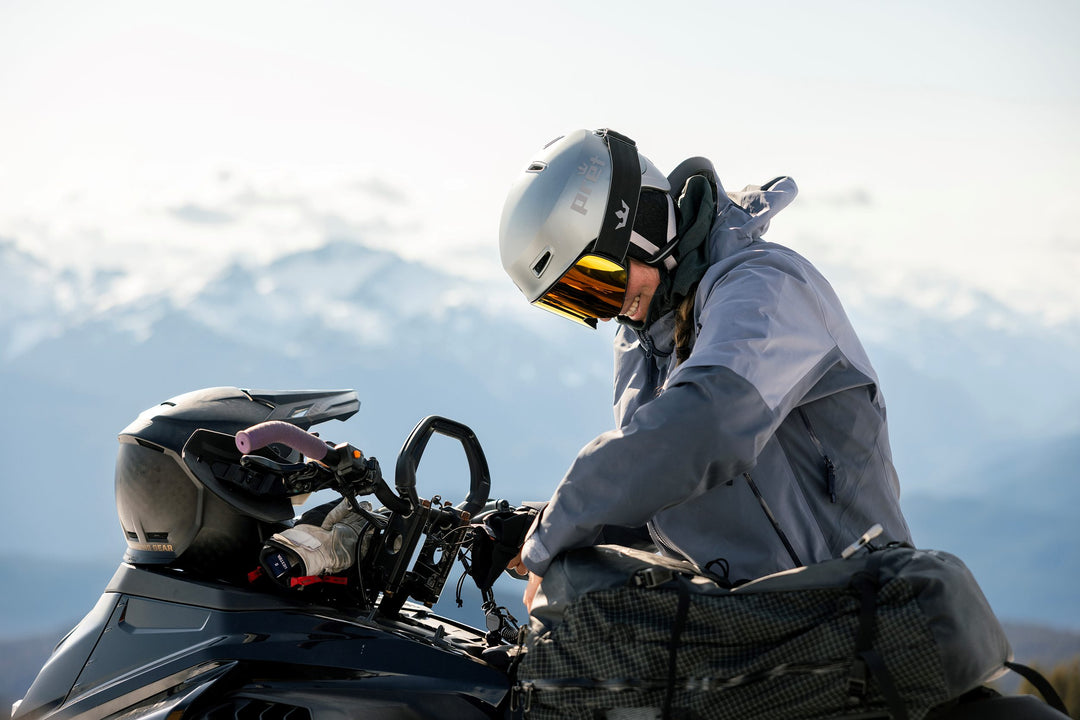 Person wearing a helmet sitting on a snowmobile with mountains in the background