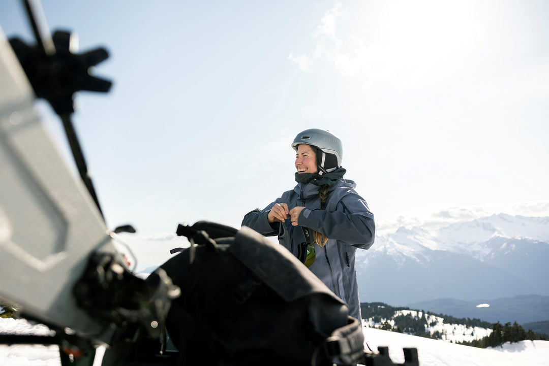 Person in winter gear standing on a snowy landscape with mountains in the background