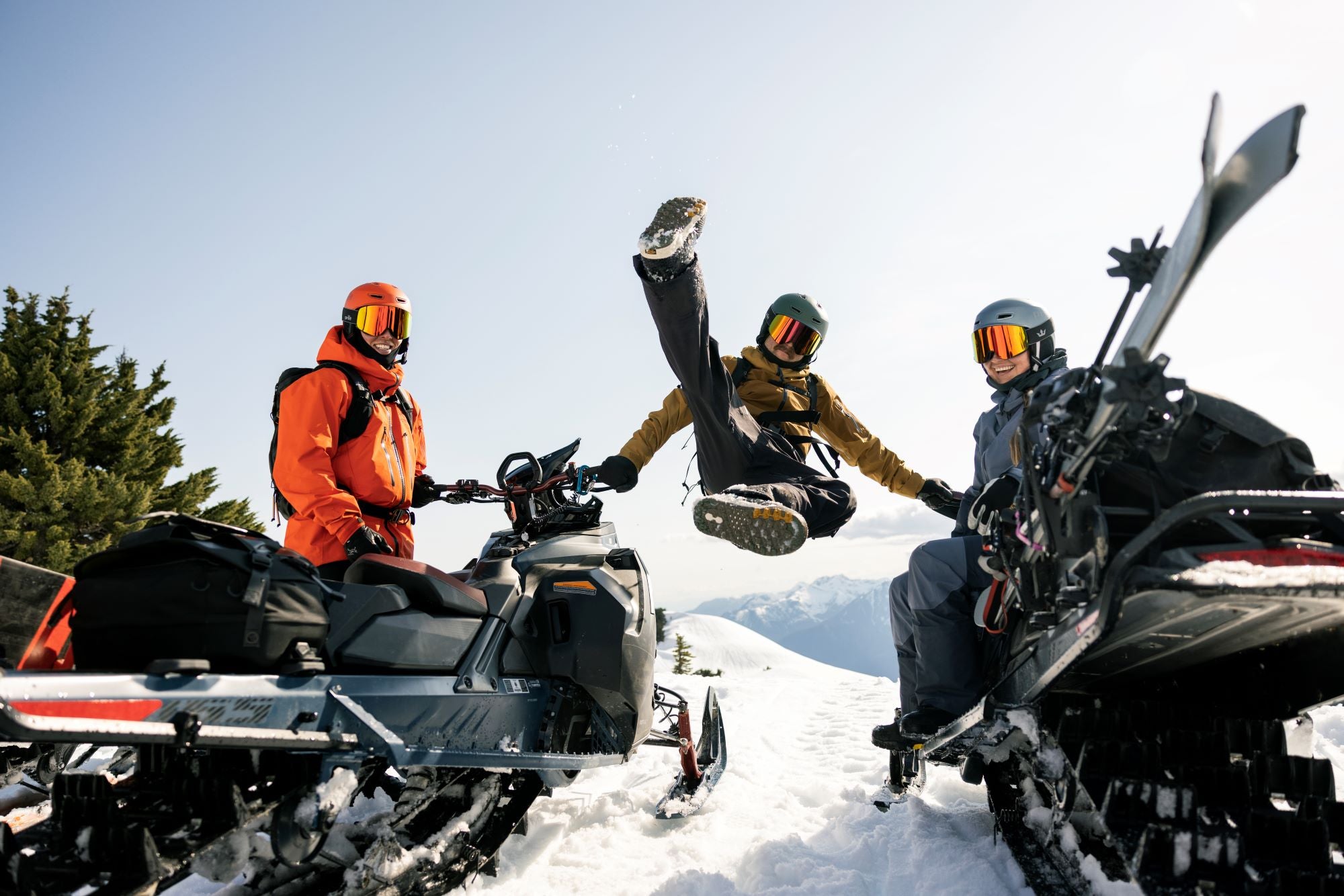 Three snowmobilers on a snowy landscape with clear blue sky
