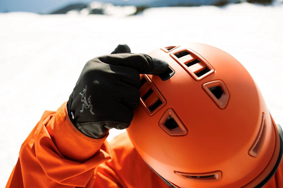 Person wearing an orange helmet and black gloves adjusting ski helmet vents