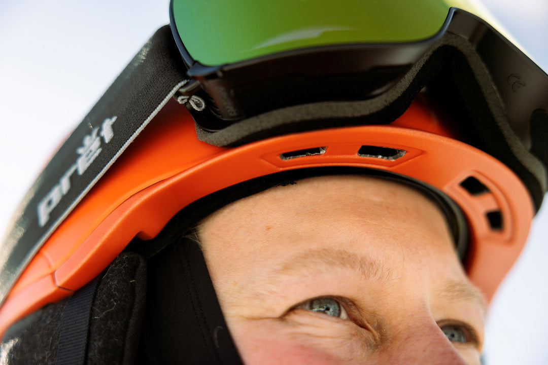 Close-up of a person wearing an orange helmet with a brand logo, against a blurred background.
