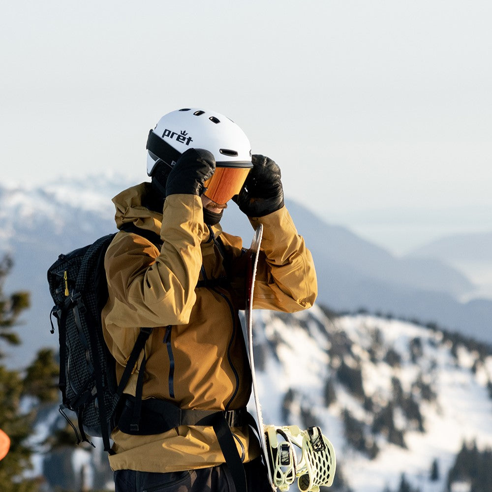 Person in yellow jacket and white helmet with goggles, standing against a snowy mountain backdrop