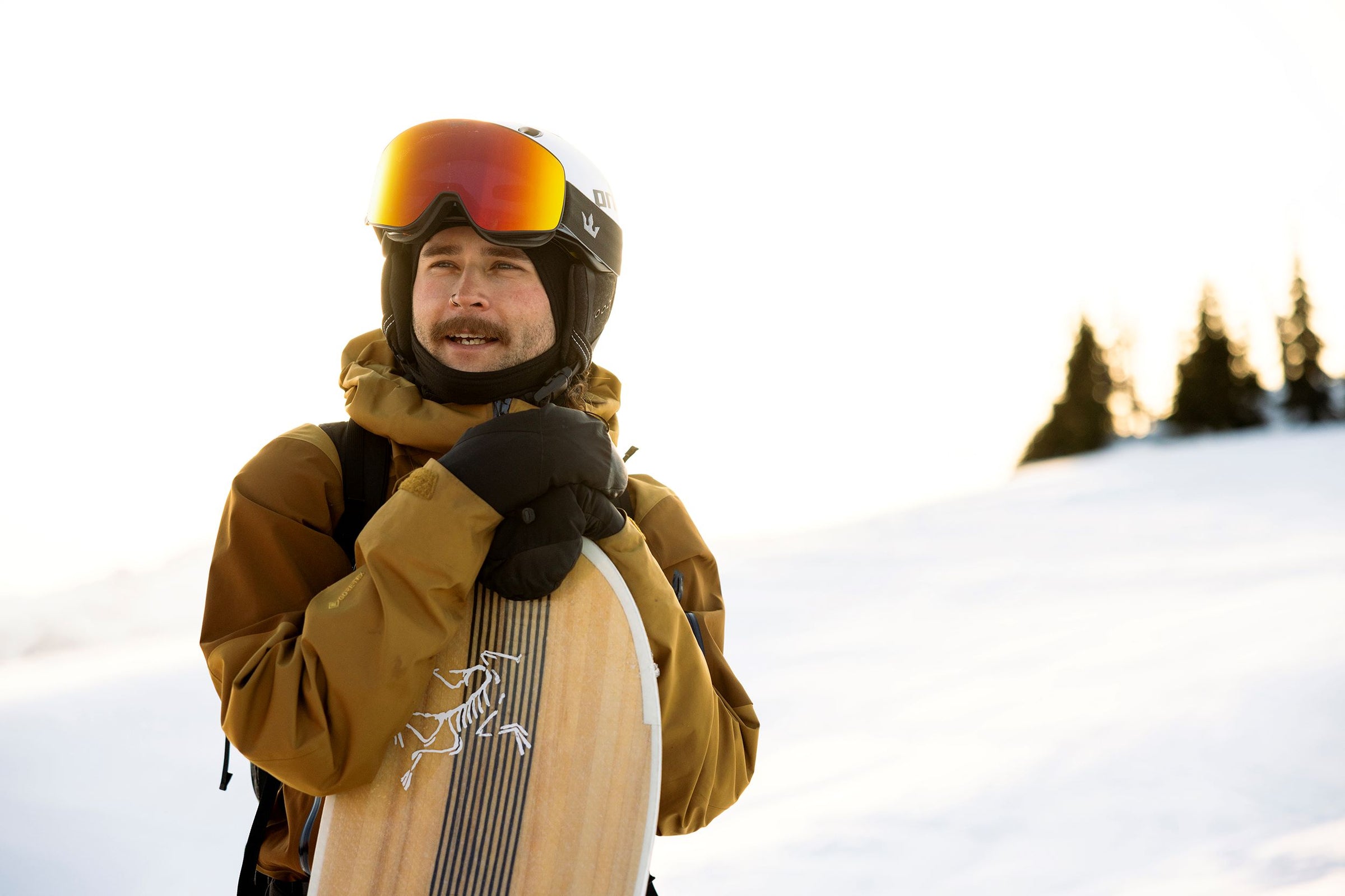 Person in winter gear with a snowboard, standing on a snowy landscape.