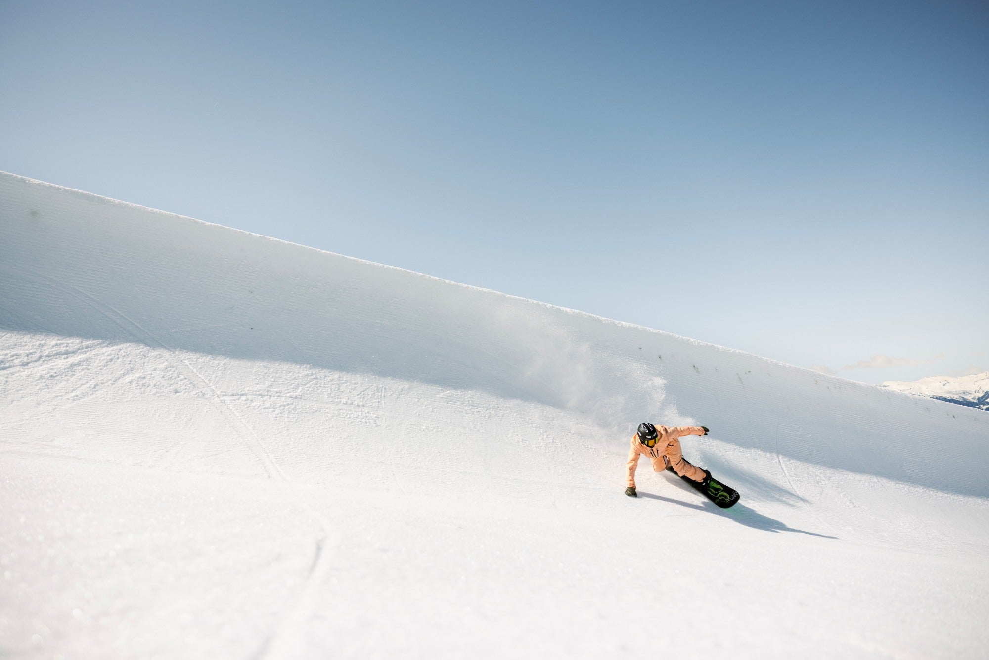 Person wearing helmet snowboarding down a snowy slope with a clear blue sky