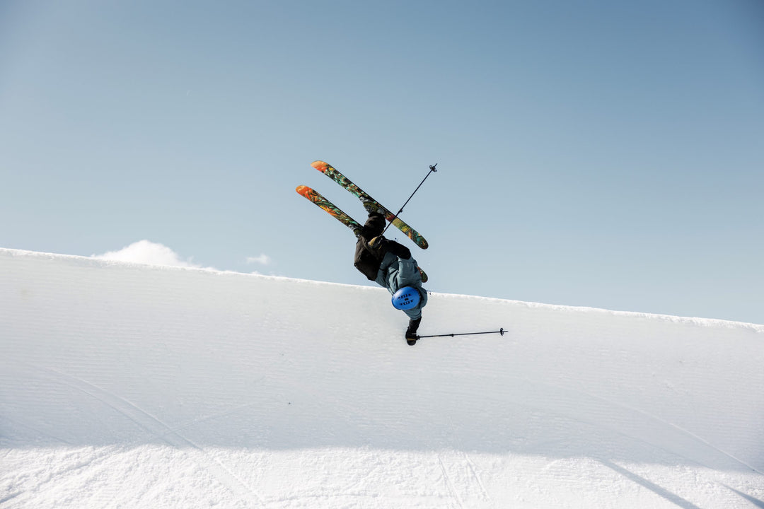 Skier performing a trick in the air on a snowy slope with a clear blue sky.