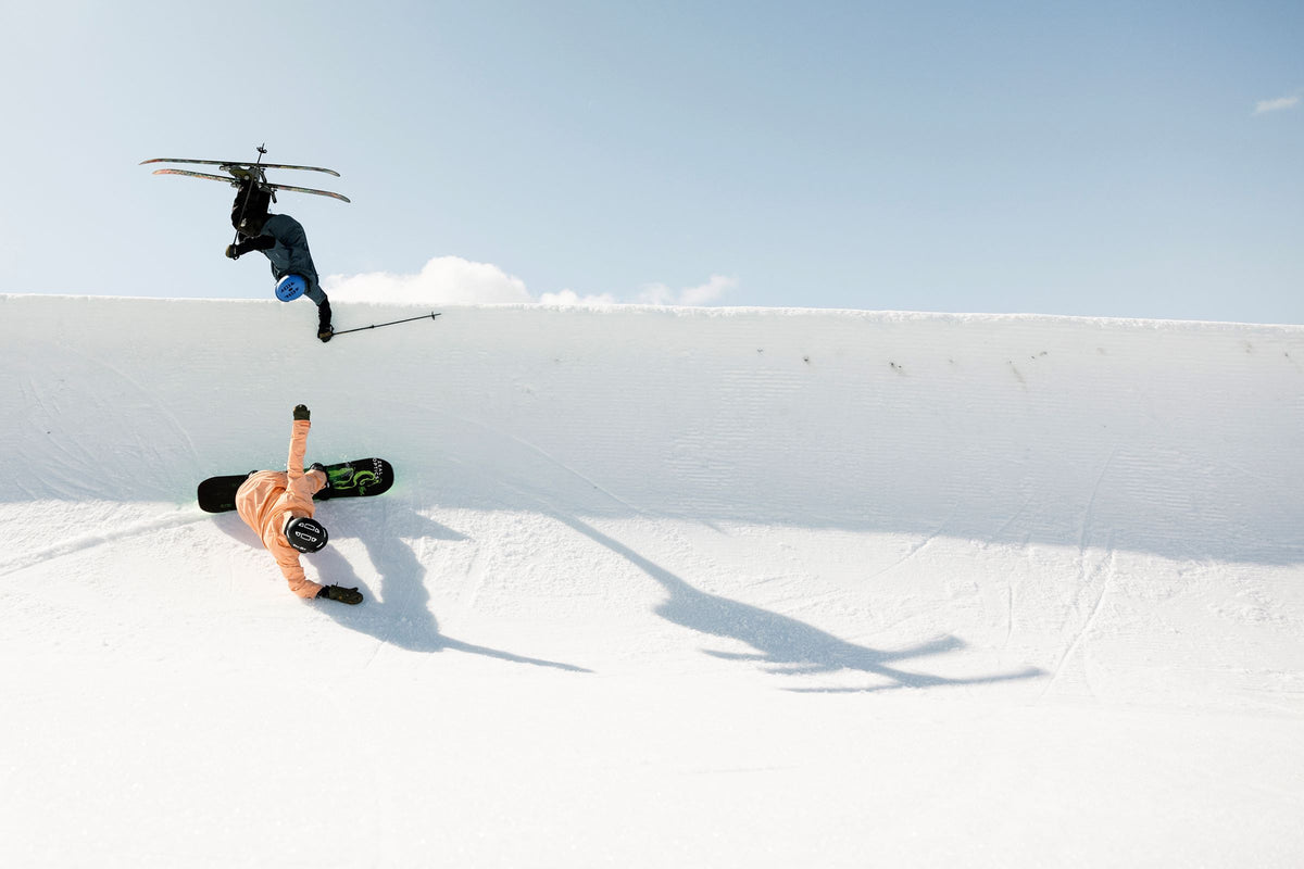 snowboarder on half pipe and skier midair of a jump off side of half pipe. Blue sky in background