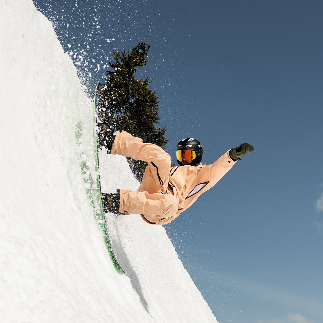 person snowboarding on a half pipe in a black helmet and a peach snowsuit