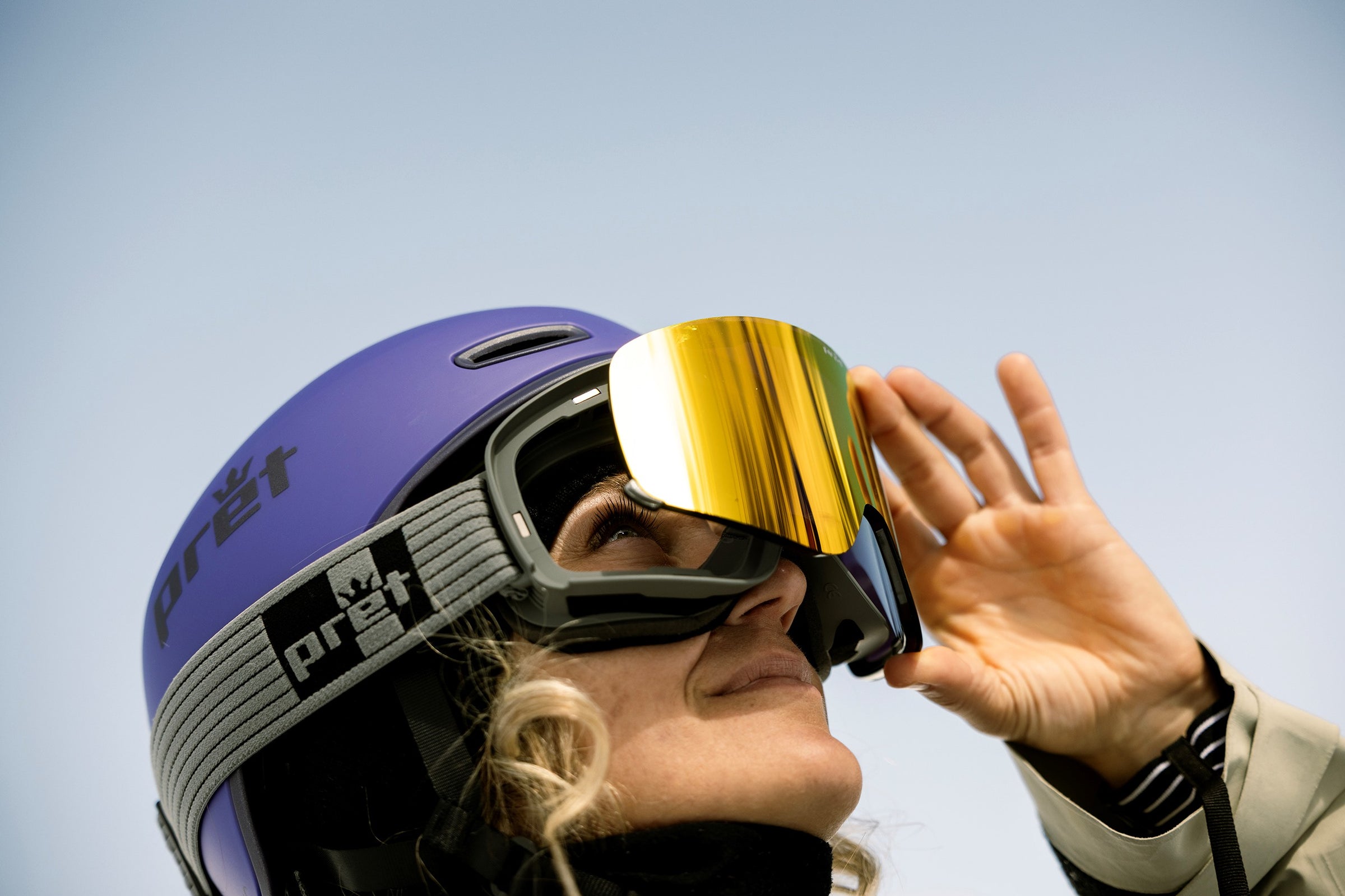 Person wearing a purple helmet with reflective goggles against a clear blue sky