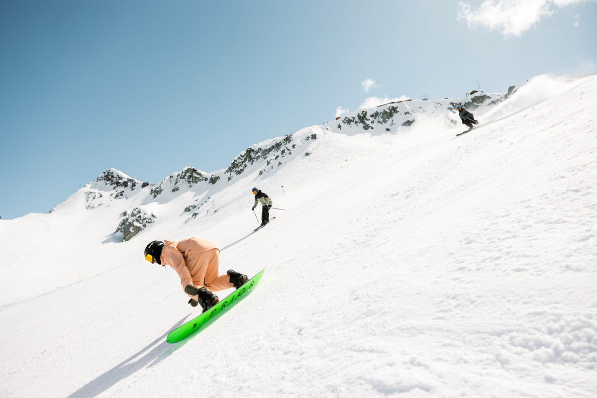 Person snowboarding down a snowy slope with skiers and mountains in the background