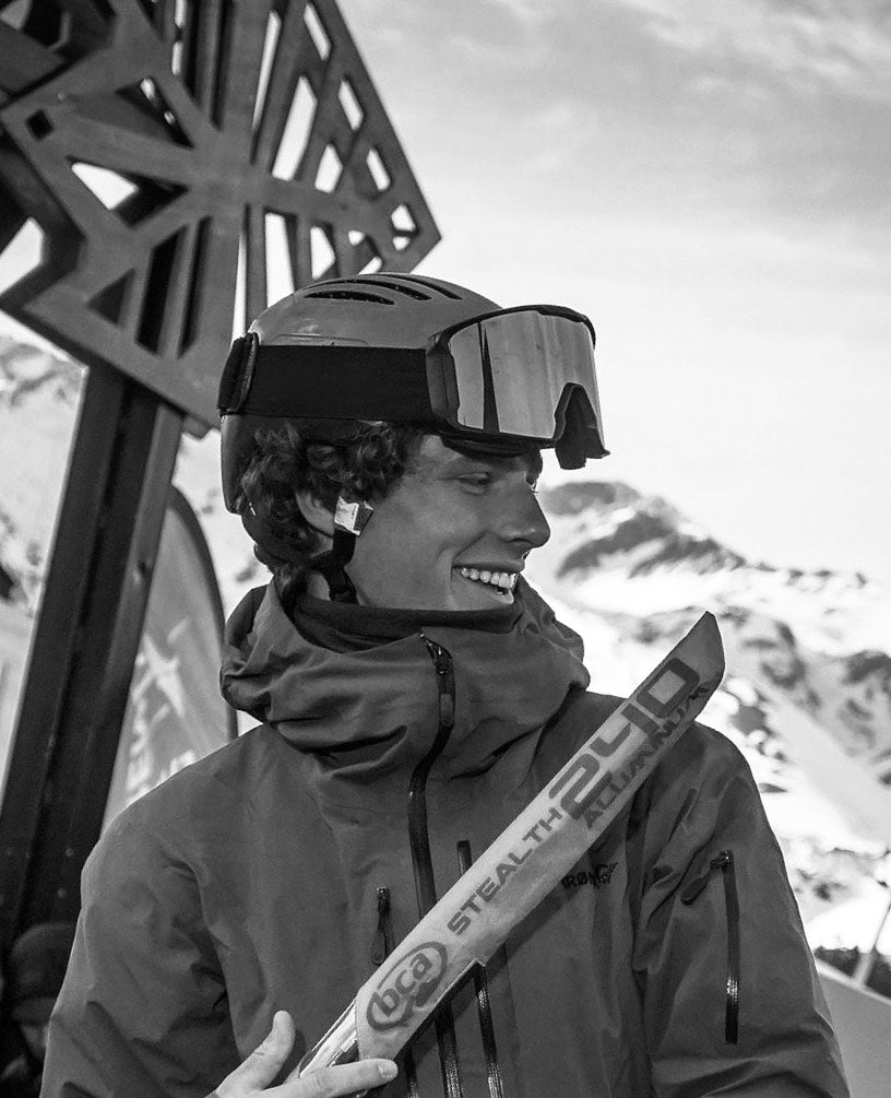 Christopher Noone wearing ski goggles and holding a ski with a mountain background