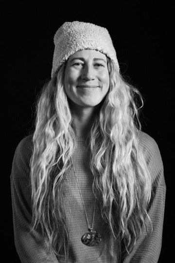 Black and white portrait of a person with long hair wearing a knitted hat against a black background
