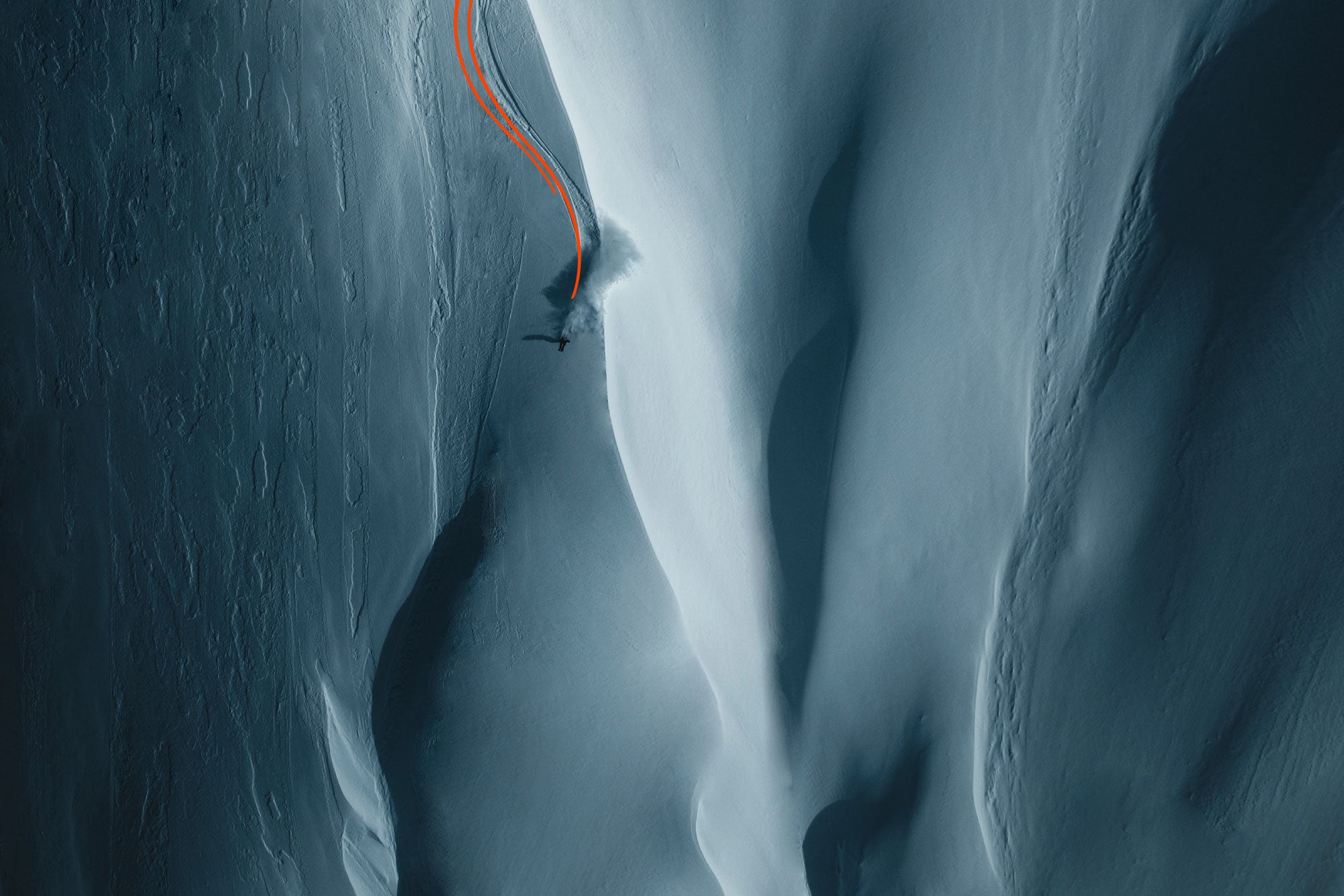 Person in the far distance skiing down a moody snow-covered mountain