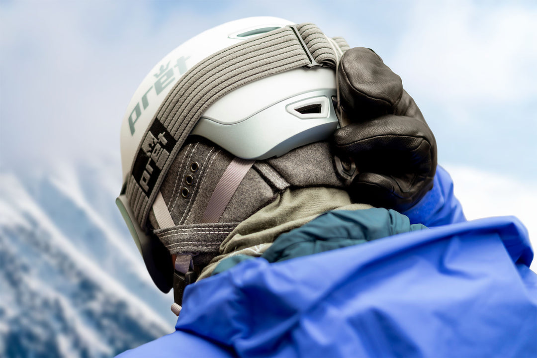 Person adjusting their helmet and wearing goggles with a snowy mountain background